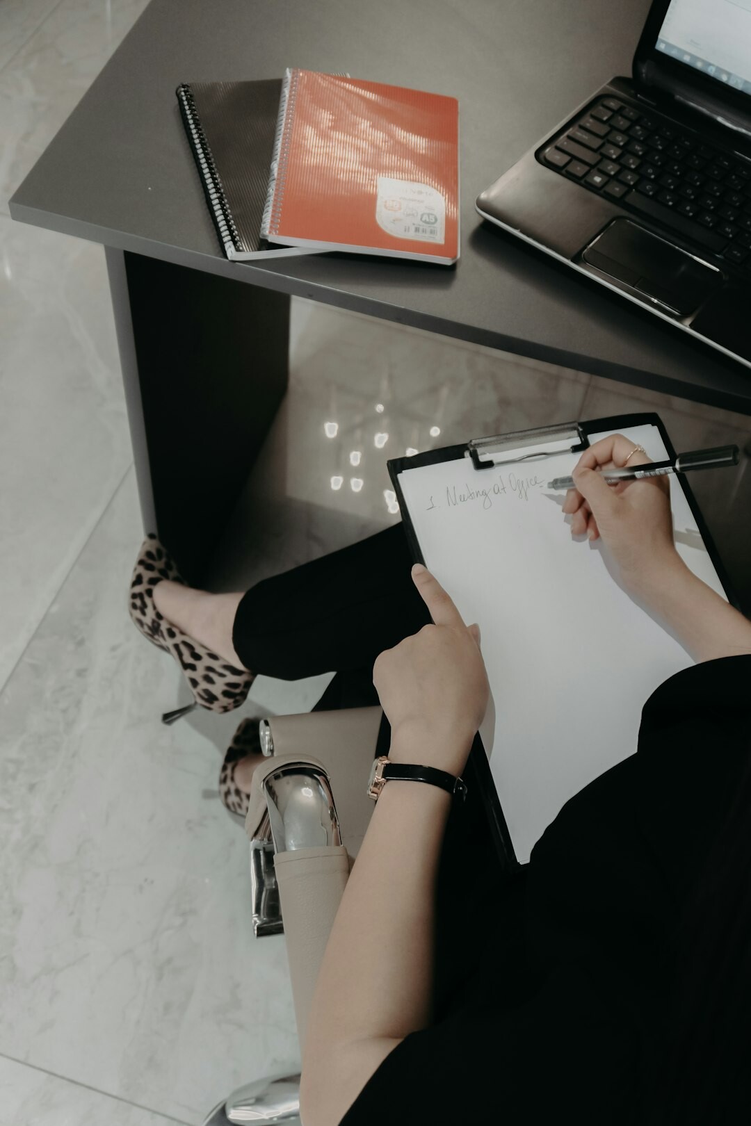 Overhead view of hands writing in a notebook next to a laptop